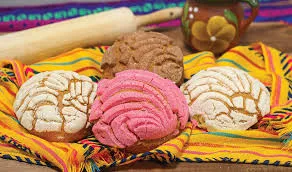 Three conchas resting on a colorful Mexican textile alongside a wooden rolling pin