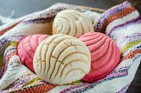 Pink and vanilla vegan conchas nestled in a woven cloth basket