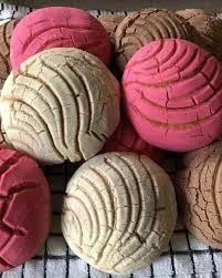 Pink and vanilla vegan conchas cooling on a wire rack, showing the colorful candy-shell scoring