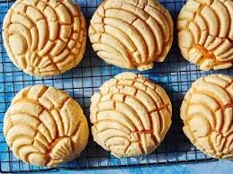 A golden batch of vanilla vegan conchas arranged on a blue cooling rack